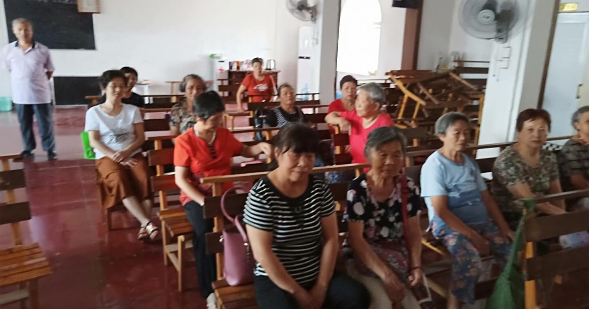 A group of people is sitting on benches in what appears to be a small church.