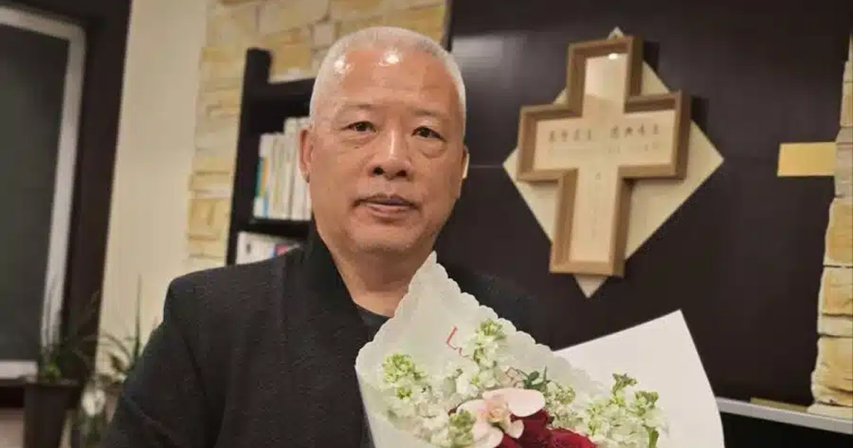 Elder Zhang Chunlei is holding a large bundle of flowers. There is a cross on the wall behind him.