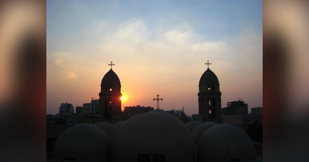 Three crosses on Coptic steeples are silhouetted against the sun on the horizon.