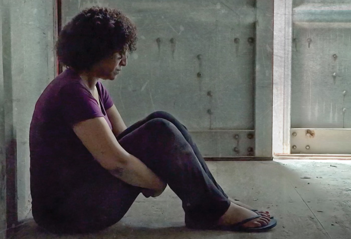 Screenshot of reenactment - Helen Berhane is sitting on the floor of a shipping container showing signs of having been beaten.