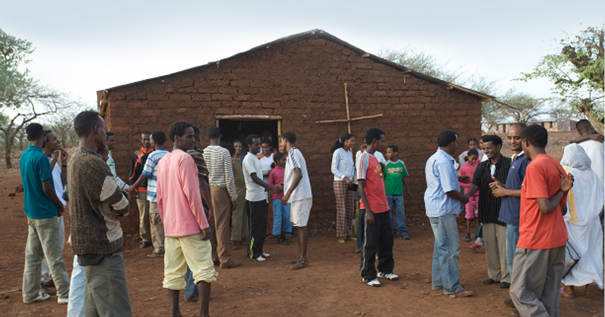 A group of people is gathered outside a small church.