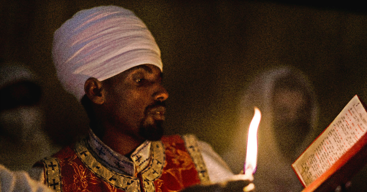 Worshippers are illuminated only by candlelight, looking at an open book. Worshippers are illuminated only by candlelight, looking at an open book.