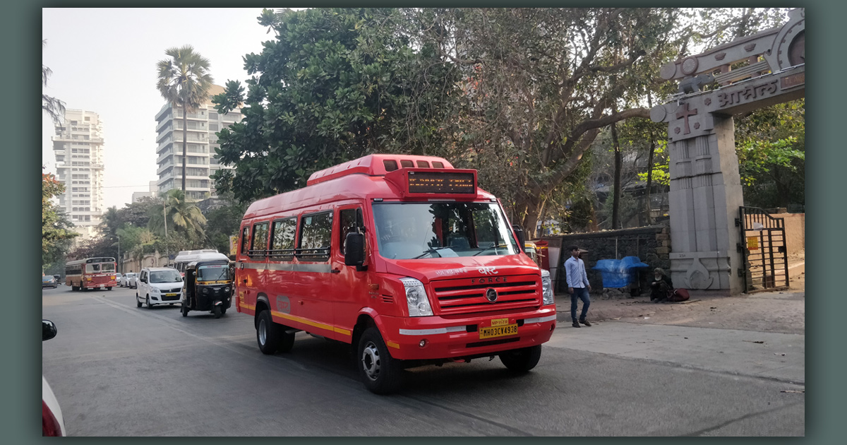 A small red bus is travelling on a street in India.