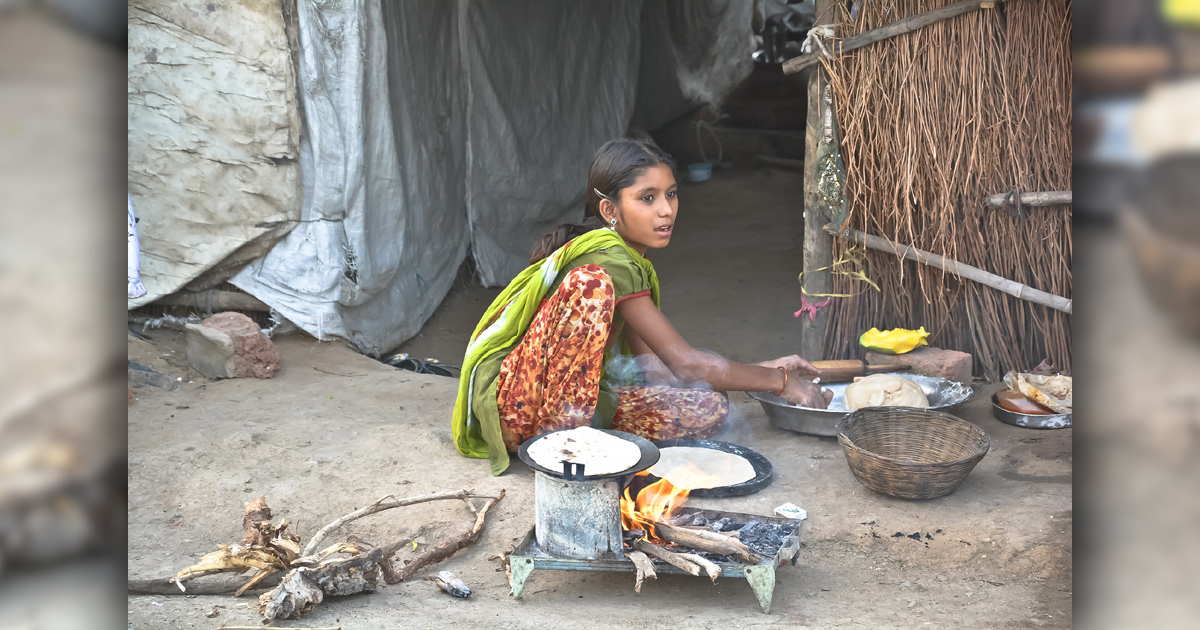 A young girl cooking over an open fire just outside her home.