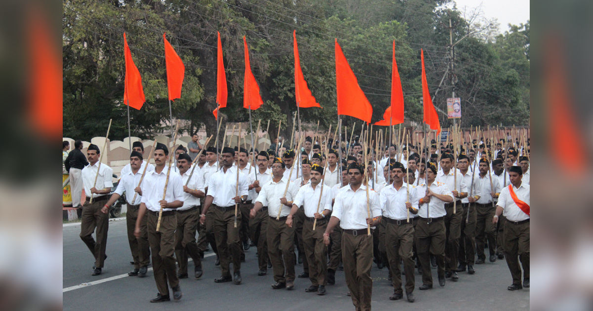 A group of men in white shirts are carrying orange flags and marching through the street.