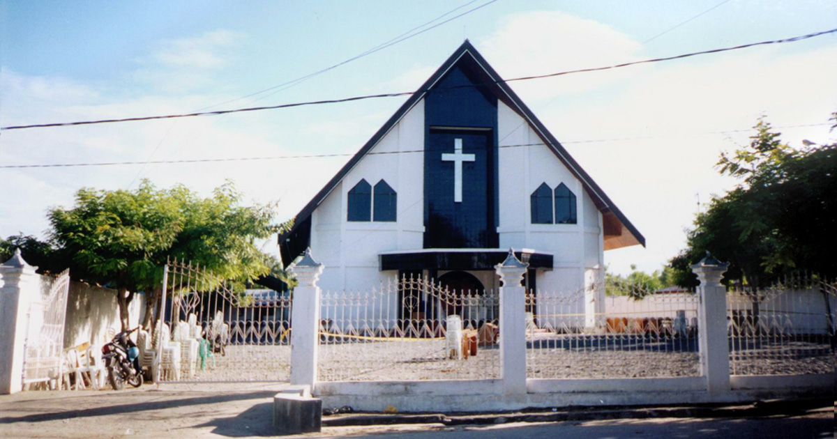 A white church with blue trim clearly displays a cross on the front. 