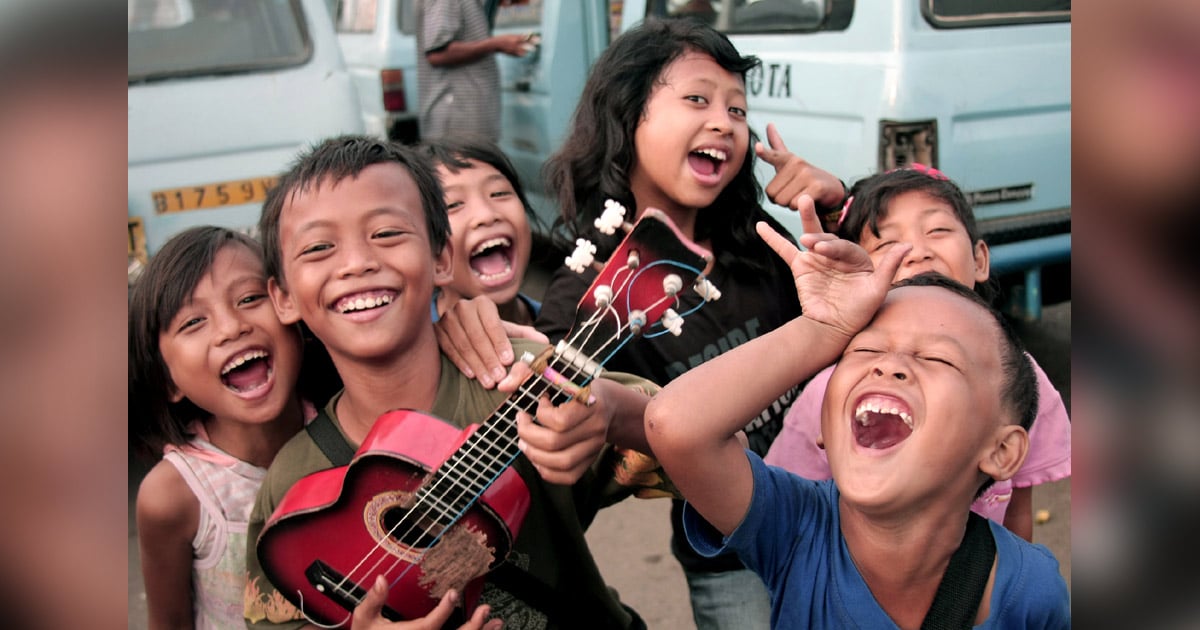 A group of children are smiling and laughing. One is playing an ukulele.