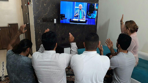 Christians worshipping at home; the leader is on TV.