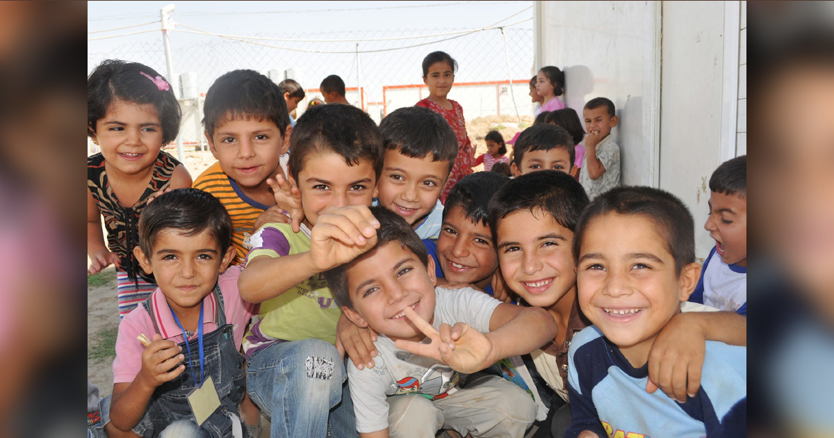 Iraqi children are huddled together, smiling and scrambling for the attention of the photographer.