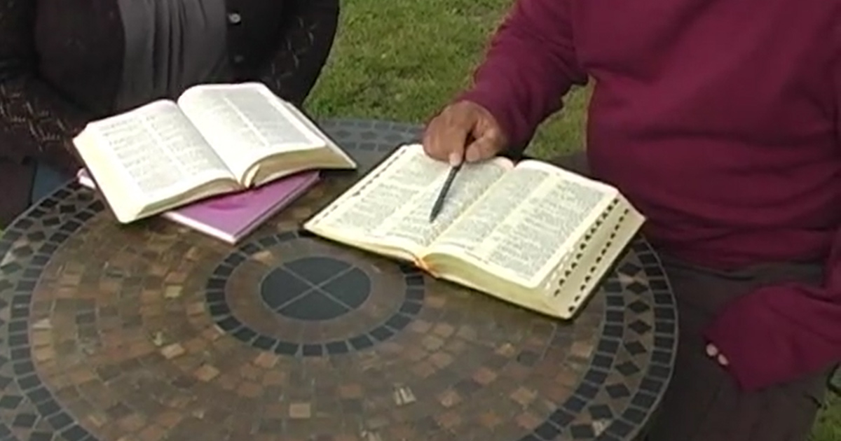Two people are studying Bibles while sitting at a mosaic style tabletop. No faces can be seen.