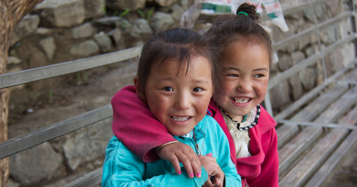Two girls in brightly coloured clothing are hugging on an outdoor bench. Two girls in brightly coloured clothing are hugging on an outdoor bench.