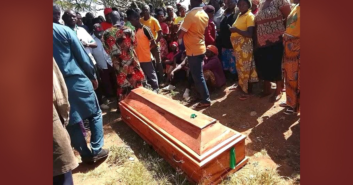 Mourners are gathered around a casket that is resting on the ground. Mourners are gathered around a casket that is resting on the ground.