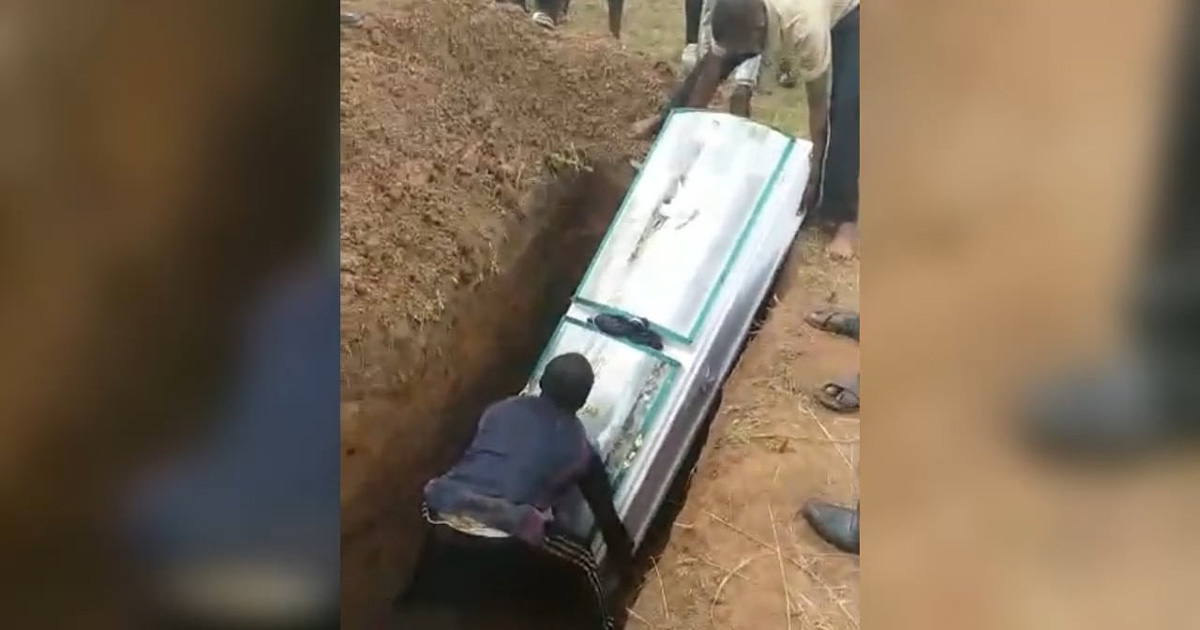 Two men are lowering a casket into the ground.