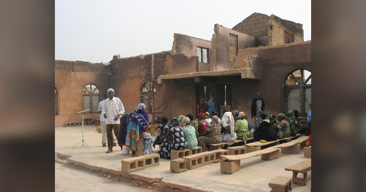 Church members are seated on cinder blocks in a burned out church. Church members are seated on cinder blocks in a burned out church.
