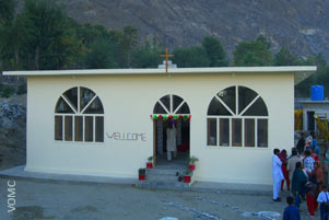 A small church building. A group of people are gathered to one side.