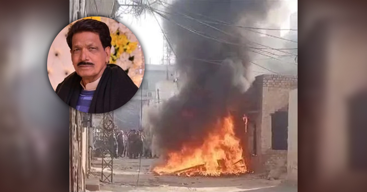 A fire is burning in the street. People are milling about in the background. Nazir Masih's photo is also in a corner of the image.