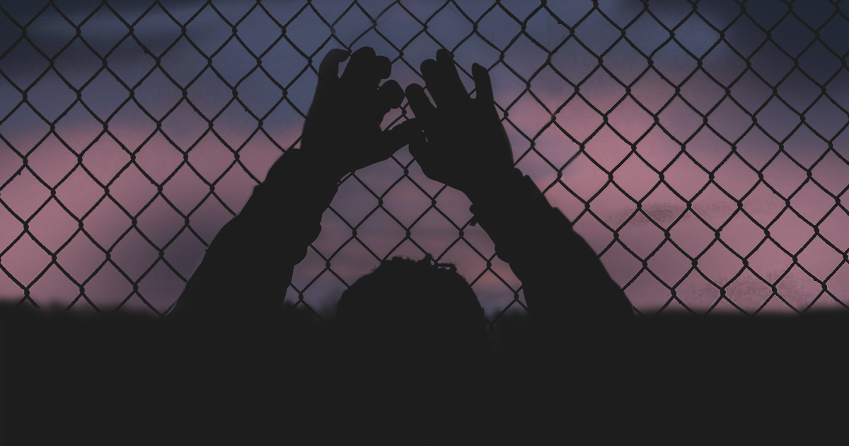 A silhouette of a man gripping a chain link fence.