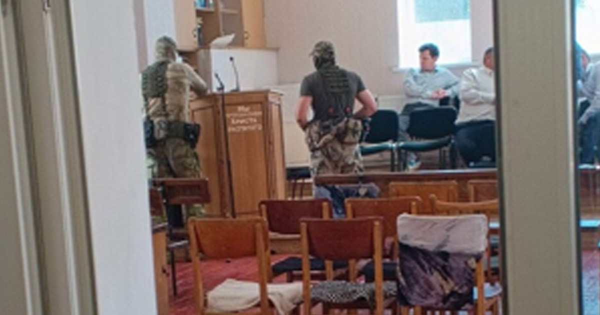 Police are roaming through a church building while church members sit on the stage.