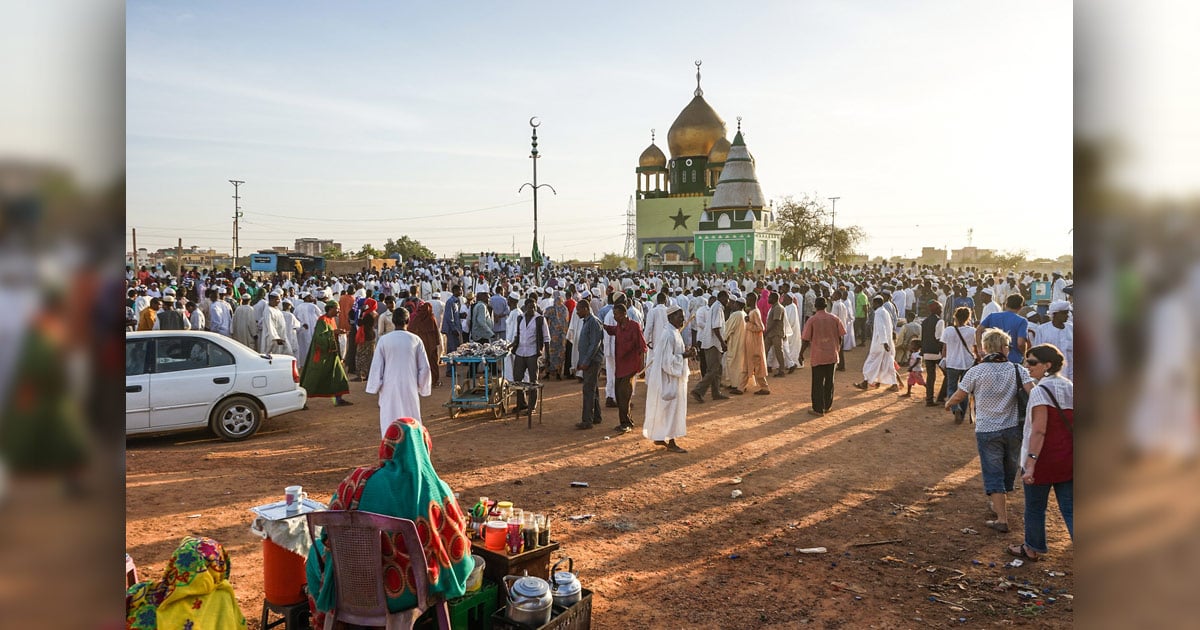 A large group of people are gathered around a small mosque.