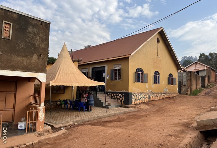 A village street is lined with buildings. People are gathering under a canopy.