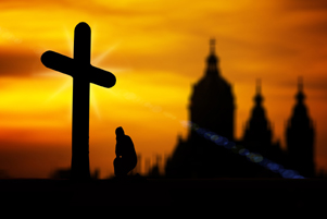 A sillhouette of a cross, a man praying and a church in the background - Photo: Pixabay / Geralt