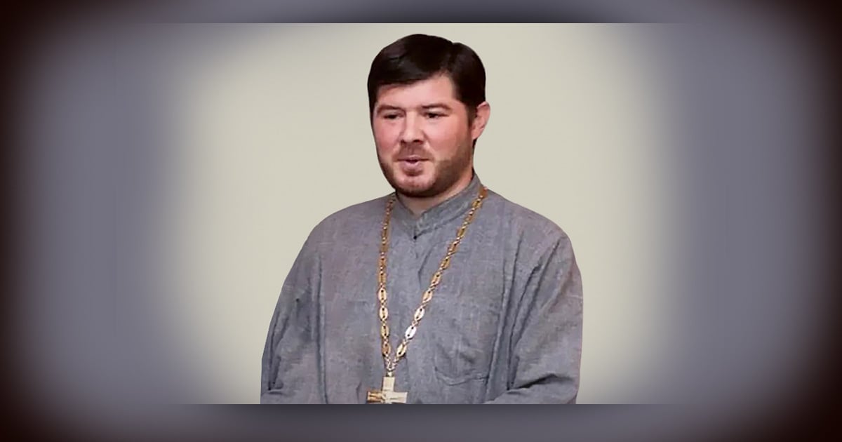 Father Kostiantyn Maksimov in a grey robe. He is wearing a large cross around his neck.