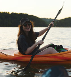 A woman is smiling, paddling a kayak.