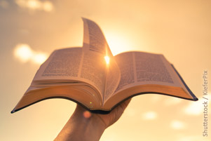 A Bible is being held up against bright sunlight.