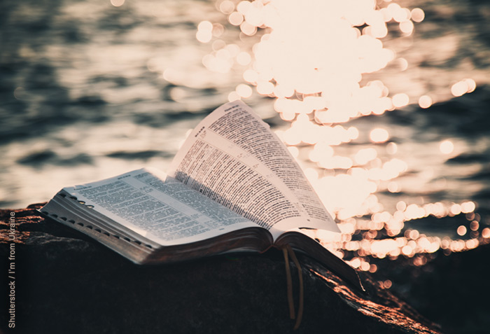 Open Bible on a rock; water with the reflection of the sun in the background