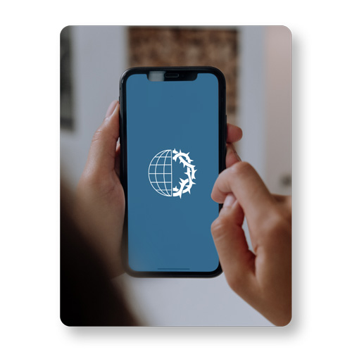 A person is holding a cell phone. The VOMC logo is on the screen.