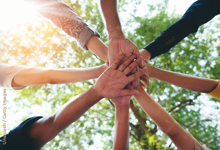 A group of hands are seen one on top of another against the sunlight bursting through tree brances. A group of hands are seen one on top of another against the sunlight bursting through tree brances.