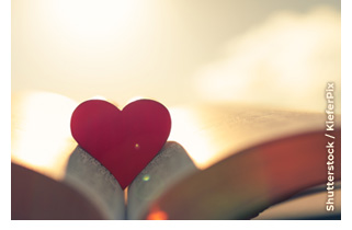 A red heart shape rests in an open Bible.