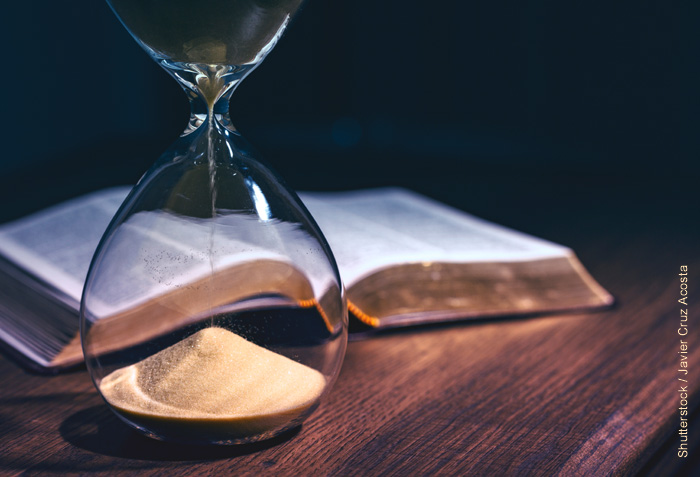An hourglass is nearly out of sand. A Bible is open just behind the hourglass.