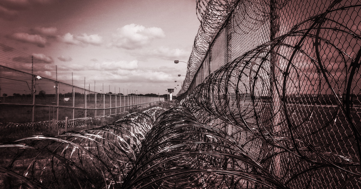 A prison fence with three rows of rolled barbed wire.