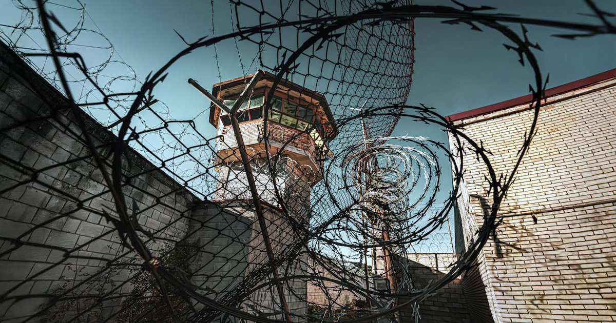 A prison watch tower rises above heavy barbed wire. A prison watch tower rises above heavy barbed wire.