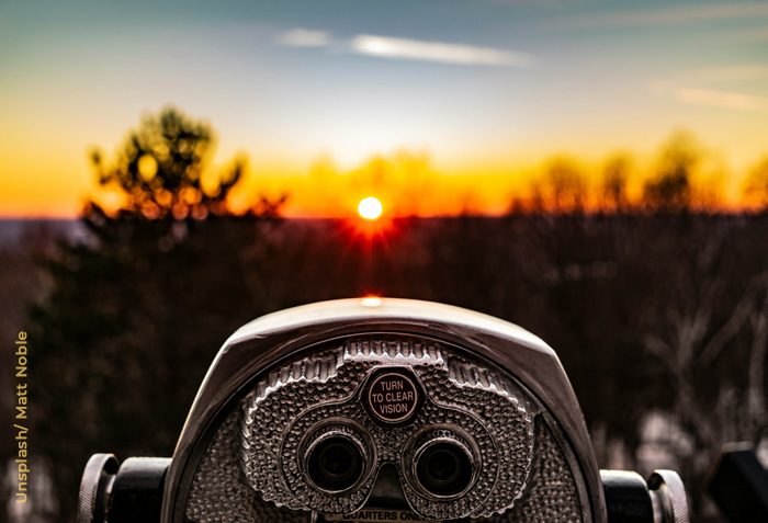 The sun is on the horizon in front of coin-operated binoculars with the label, ''Turn to clear vision.'' The sun is on the horizon in front of coin-operated binoculars with the label, ''Turn to clear vision.''