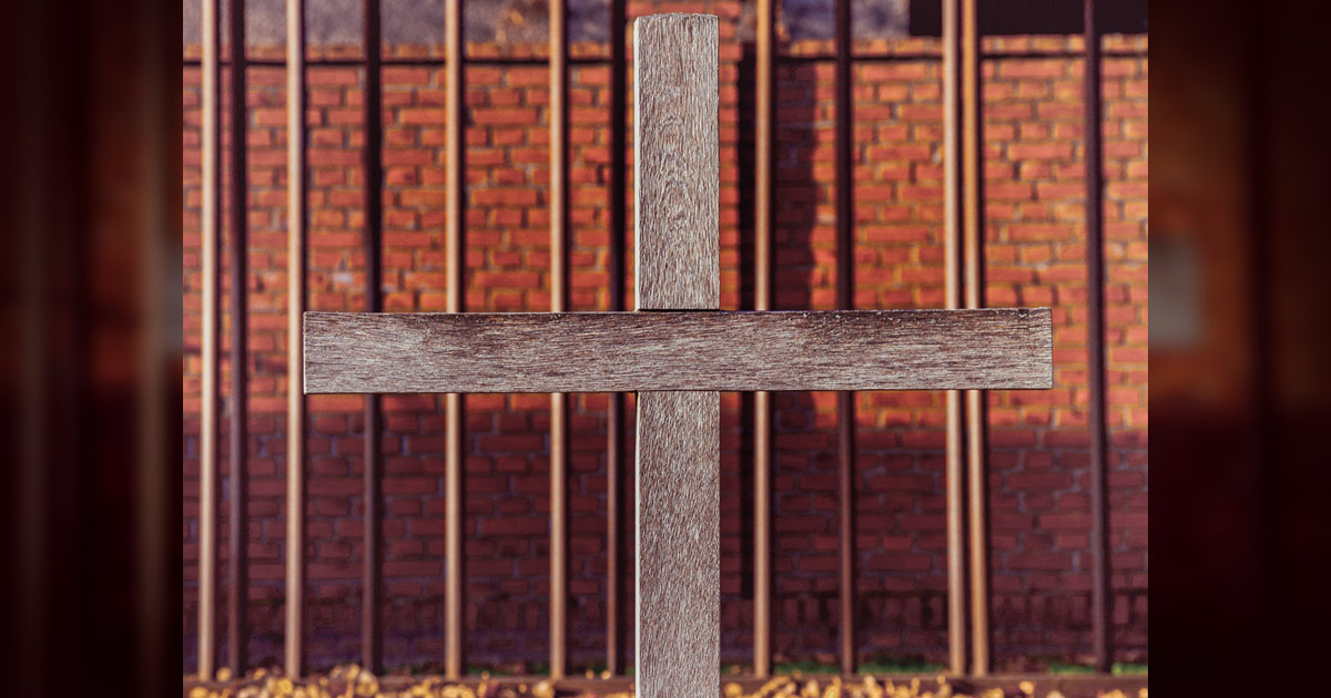 A cross with a prison wall behind it. 