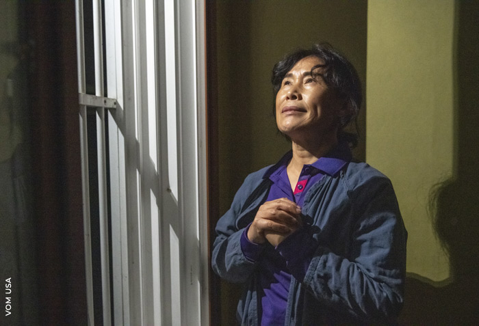  woman is praying as she looks up. She appears to be in prison.