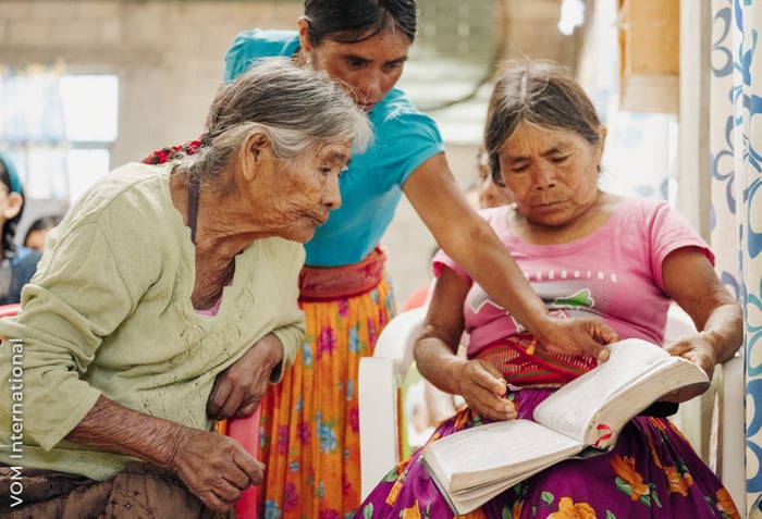 Three women are studying a single Bible together. Three women are studying a single Bible together.